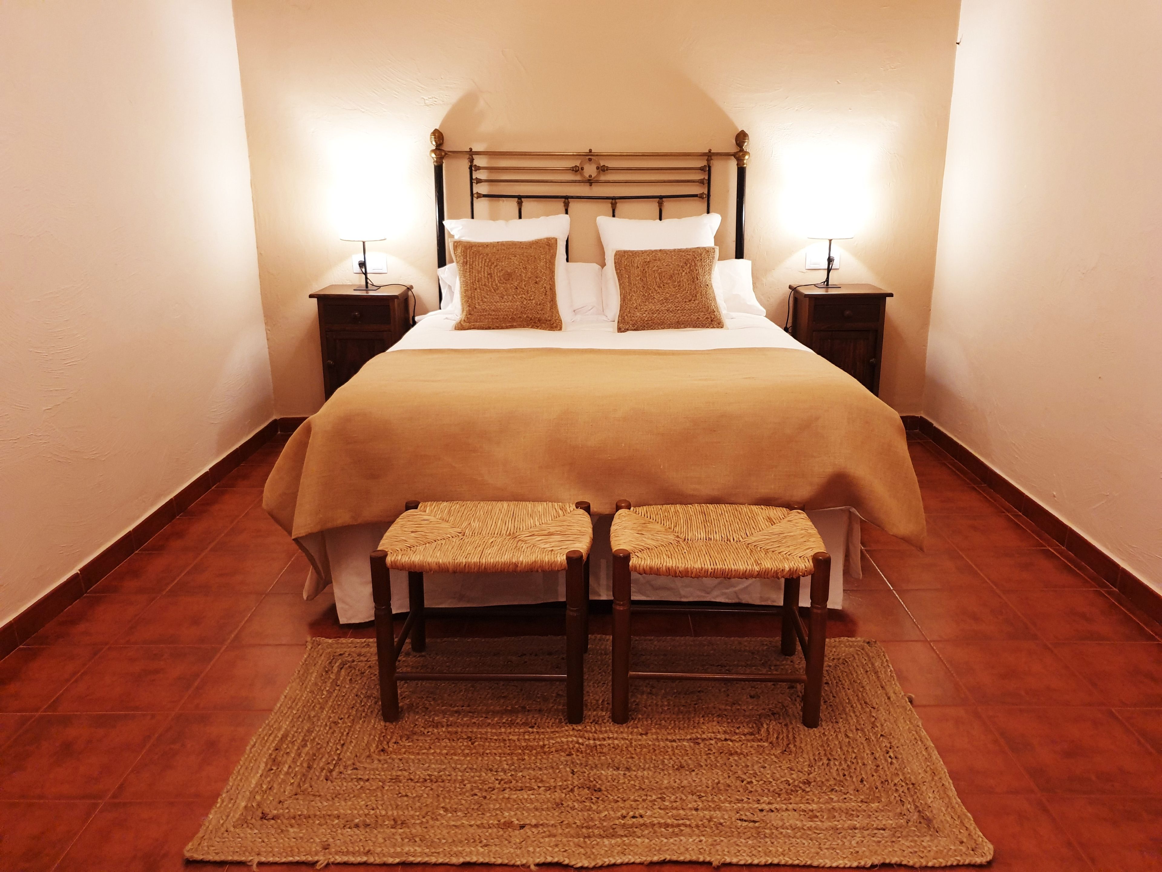 A neatly arranged bedroom with a large bed, two bedside tables, and two wicker chairs.