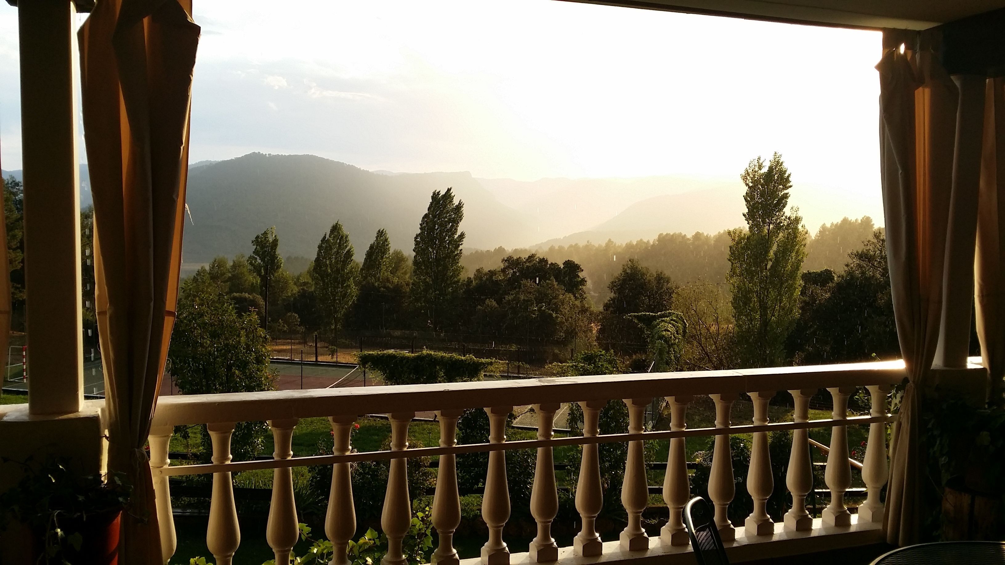 A balcony with a view of a mountainous landscape, a railing, and some greenery.