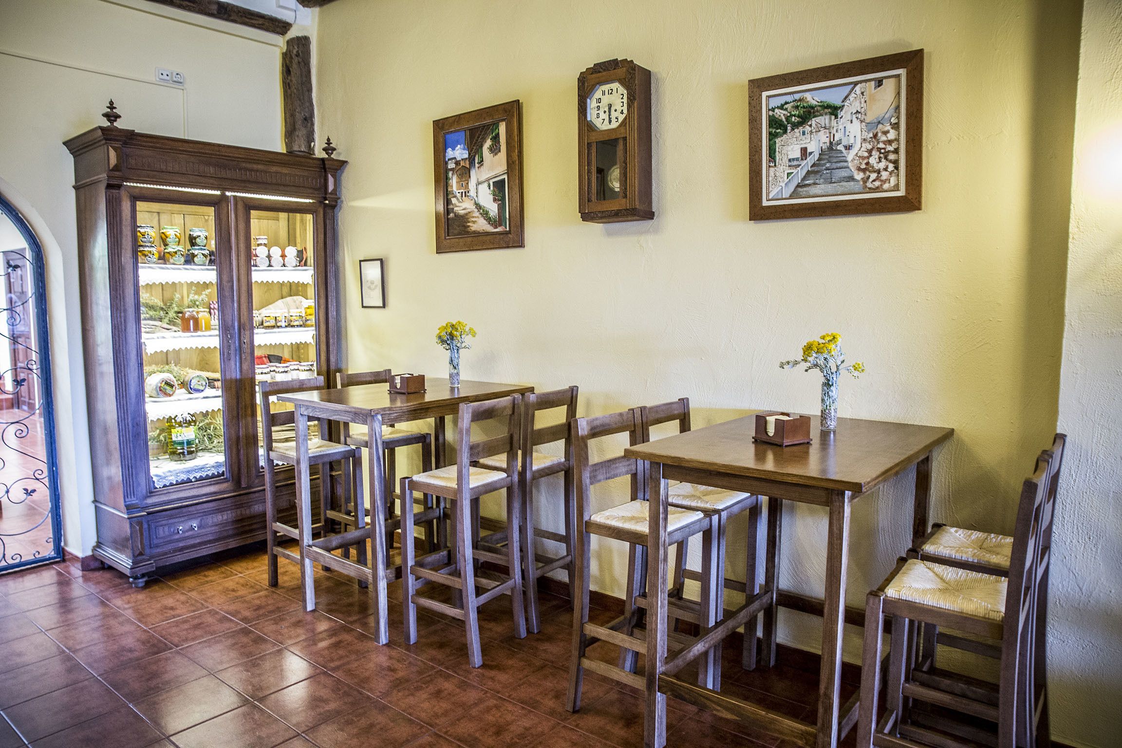 Un comedor con mesas y sillas de madera, un armario con puertas de vidrio y dos relojes de pared.