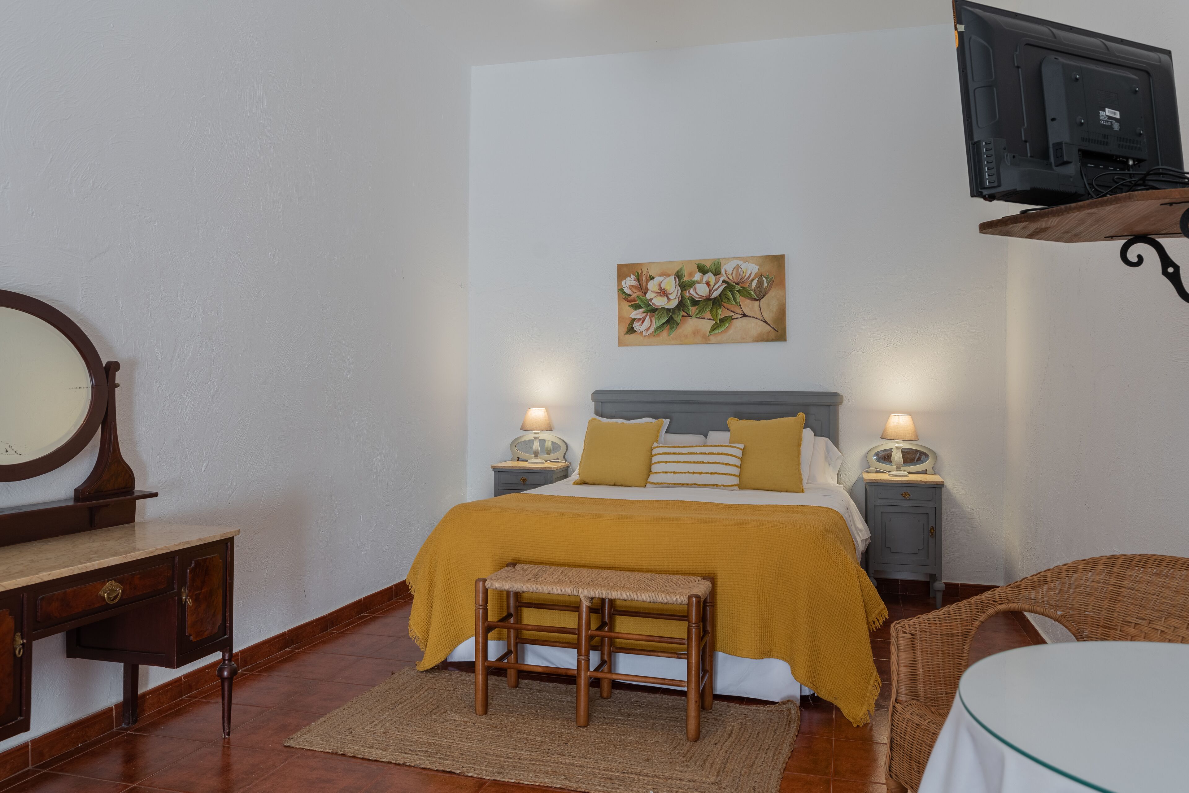 A bedroom with a bed, bedside tables, a mirror, a bench, and a television.