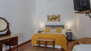 A bedroom with a bed, bedside tables, a mirror, a bench, and a television.