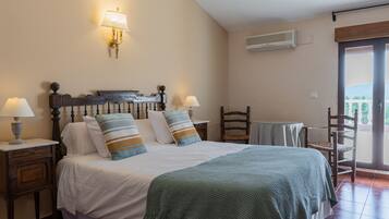 Un dormitorio con una cama, dos mesitas de noche con lámparas, una silla, una pequeña mesa y un equipo de aire acondicionado en la pared.