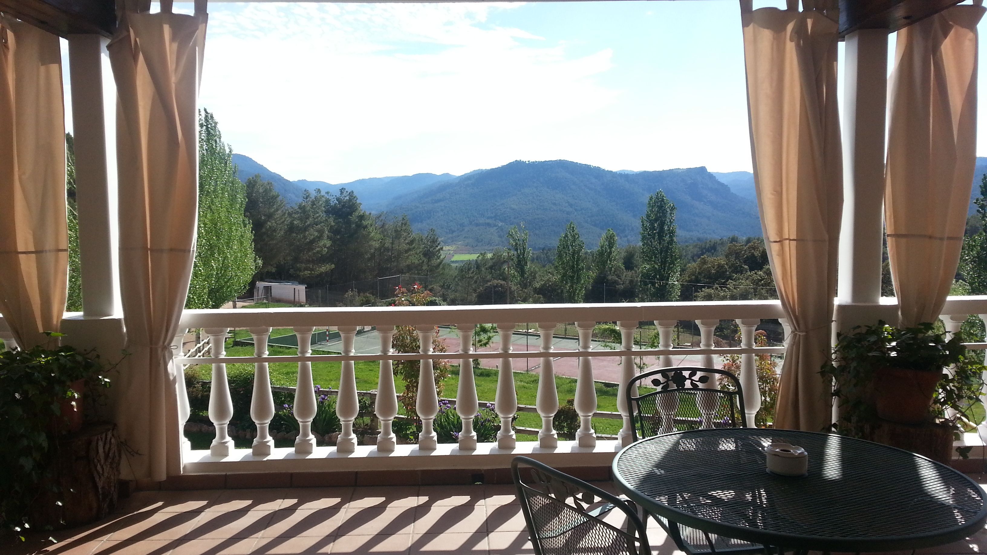 Un balcón con vistas a montañas, una mesa, sillas y plantas en macetas.