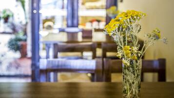 A wooden table with a vase of yellow flowers. In the background, there is a wooden cabinet with glass doors and a framed picture on the wall.