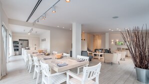 A modern, well-lit dining area with a long table, white chairs, and a potted plant. - Magical Villa in Herzliya (Herzliya)