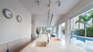 A modern kitchen with a long countertop, two wall clocks, and a view of a swimming pool outside. - Magical Villa in Herzliya (Herzliya)