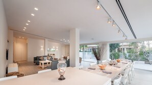 A spacious living area with a long dining table, a sofa, and a coffee table. There is a large window providing a view of the outdoors. - Magical Villa in Herzliya (Herzliya)