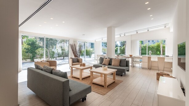A spacious living area with a sofa, coffee table, and chairs, large windows with a view of greenery, and a kitchen area with a counter and stools. - Magical Villa in Herzliya (Herzliya)
