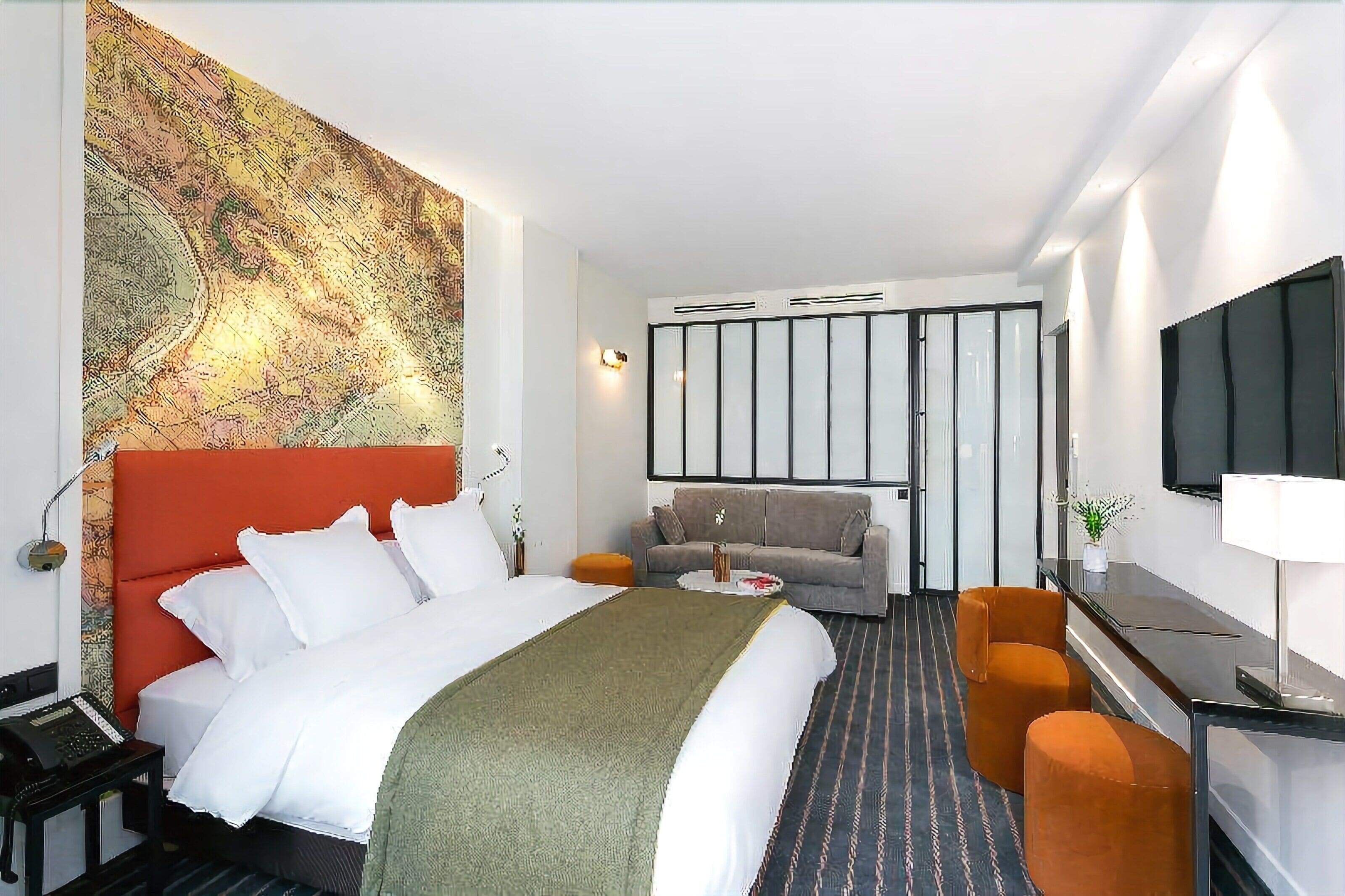 Una habitación de hotel con una cama grande, un sofá, un escritorio con televisor y un televisor montado en la pared.