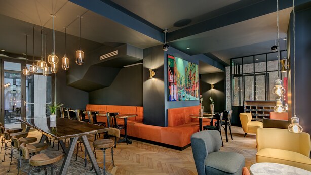 A modern lounge area with a wooden herringbone floor, seating arrangements including sofas and chairs, and pendant lighting. - Hôtel Scarlett (Paris)