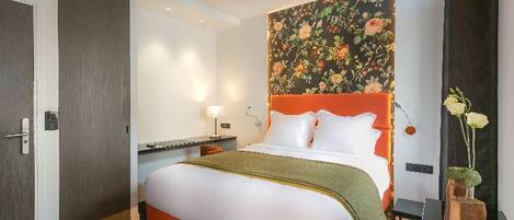Habitación de hotel con una cama grande, una mesita de noche, una lámpara y un cabecero estampado con motivos florales.