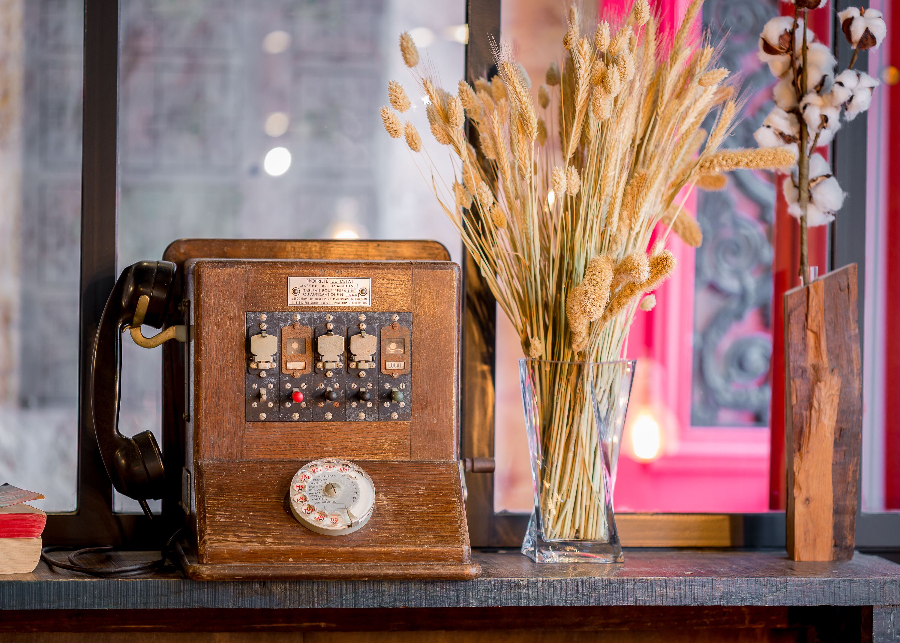 Une vieille radio posée sur une surface en bois, à côté d’un vase contenant des plantes séchées.