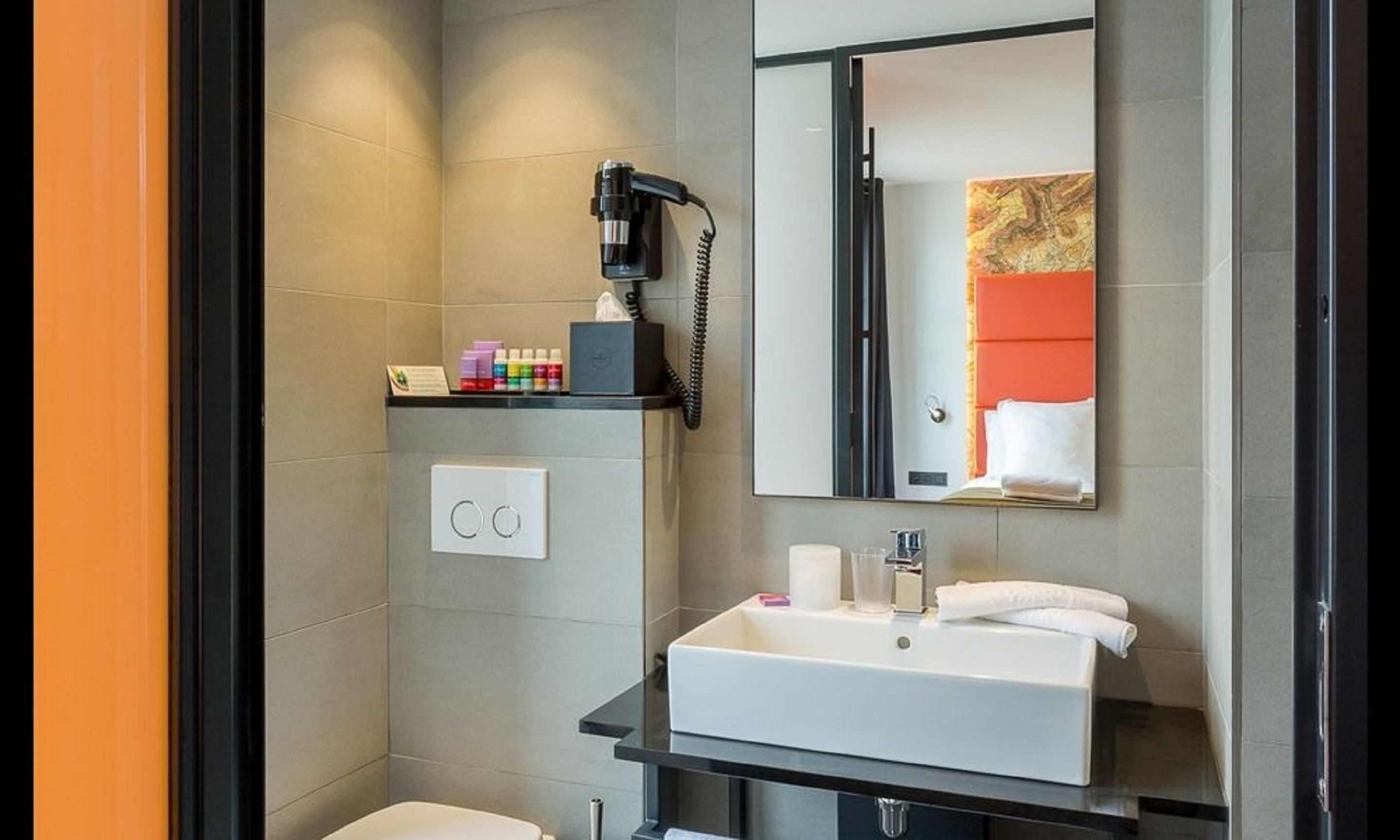 A modern bathroom with a large mirror, a white sink, and a hairdryer on a shelf.