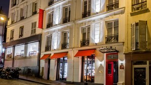 A multi-story hotel with illuminated windows and balconies, a red awning, and a visible entrance door. - Hôtel Scarlett (Paris)