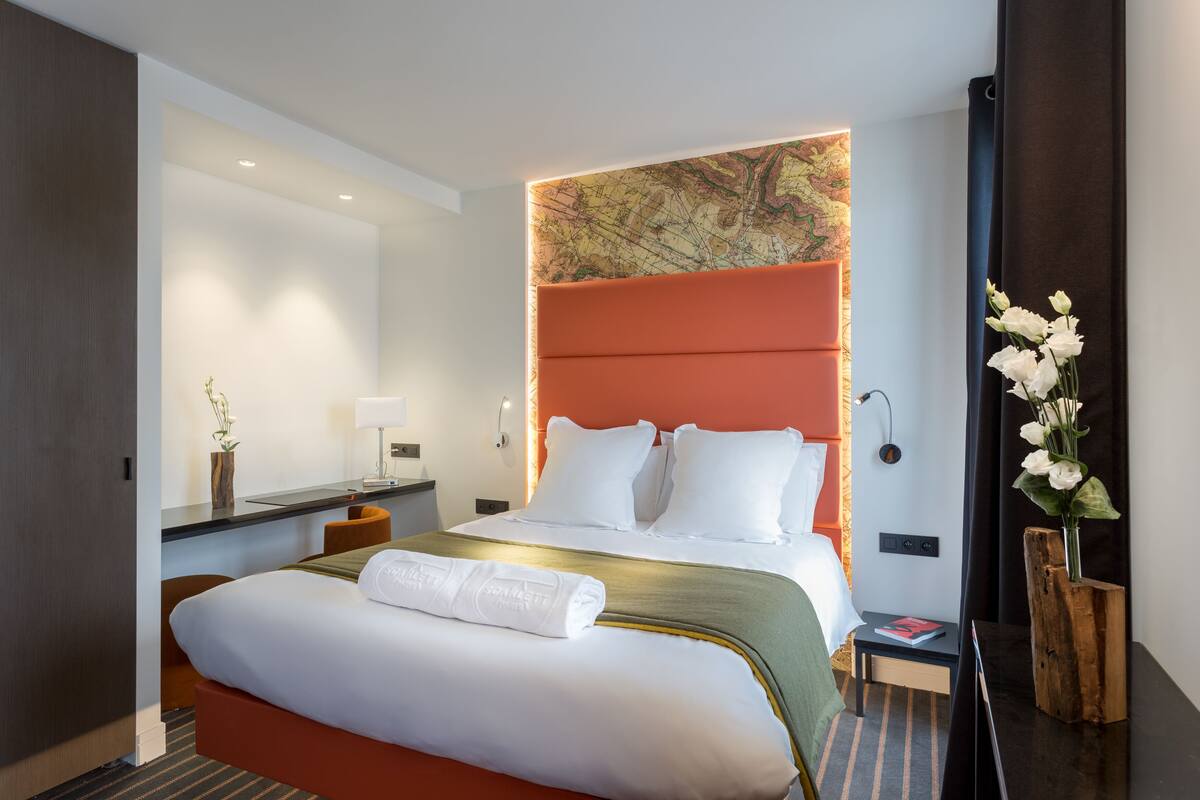 A modern hotel room with a large bed, a desk, a nightstand, and a map on the wall.