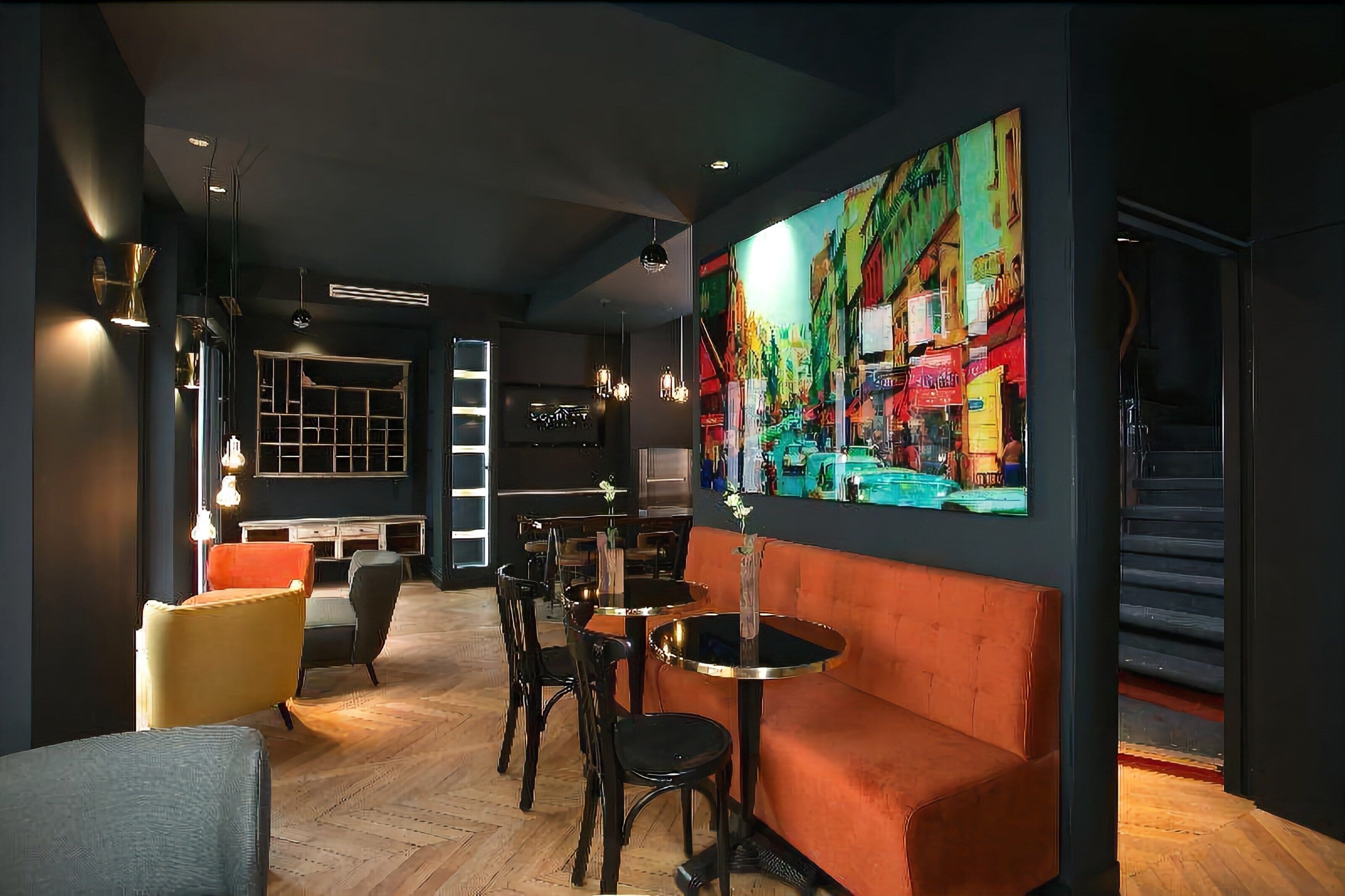 Un interior moderno con una zona de bar, diferentes disposiciones de asientos y un mural grande y colorido en la pared.