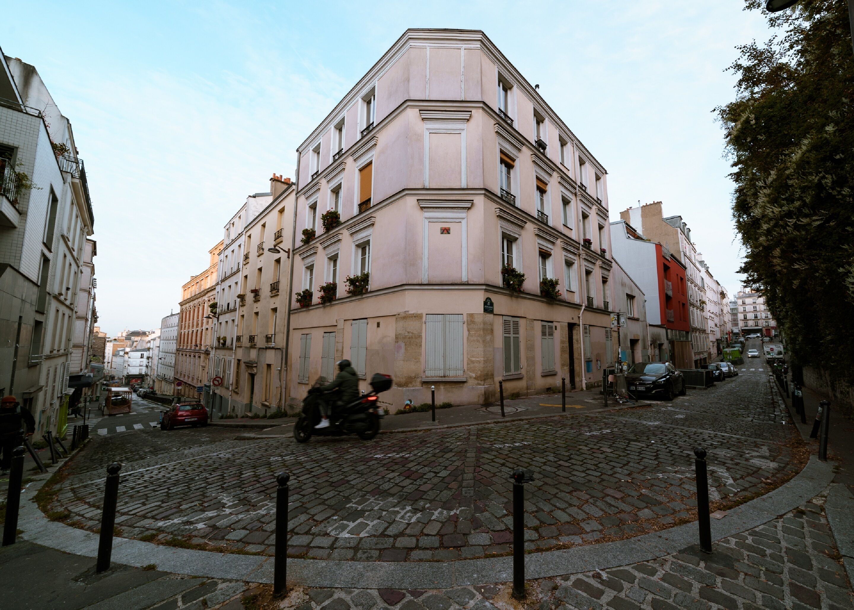 Un edificio histórico con fachada de esquina, calle adoquinada y una motocicleta pasando.
