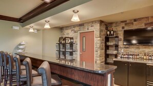 A bar area with a stone wall, a flat-screen TV, and a variety of bottles and glasses on shelves. - Cobblestone Inn & Suites - Altamont (Altamont)