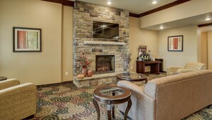 A living room with a stone fireplace, two round tables, and a sofa. - Cobblestone Inn & Suites - Altamont (Altamont)