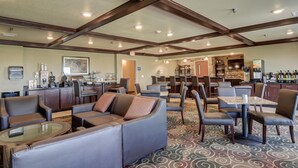 A spacious hotel lobby with a bar area, seating arrangements, and a kitchen in the background. - Cobblestone Inn & Suites - Altamont (Altamont)
