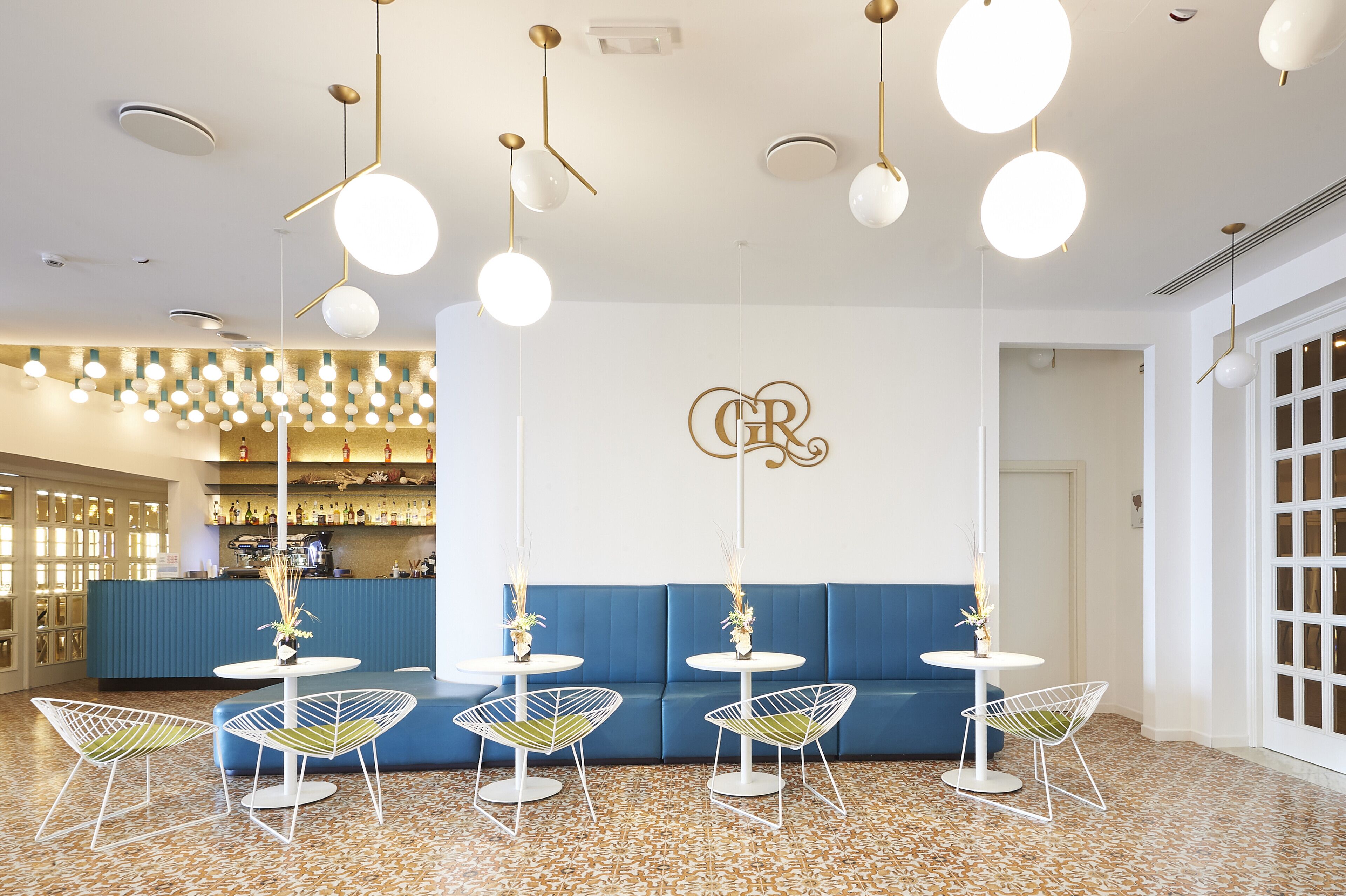 A modern interior with a blue sofa, white tables, and hanging spherical lights.