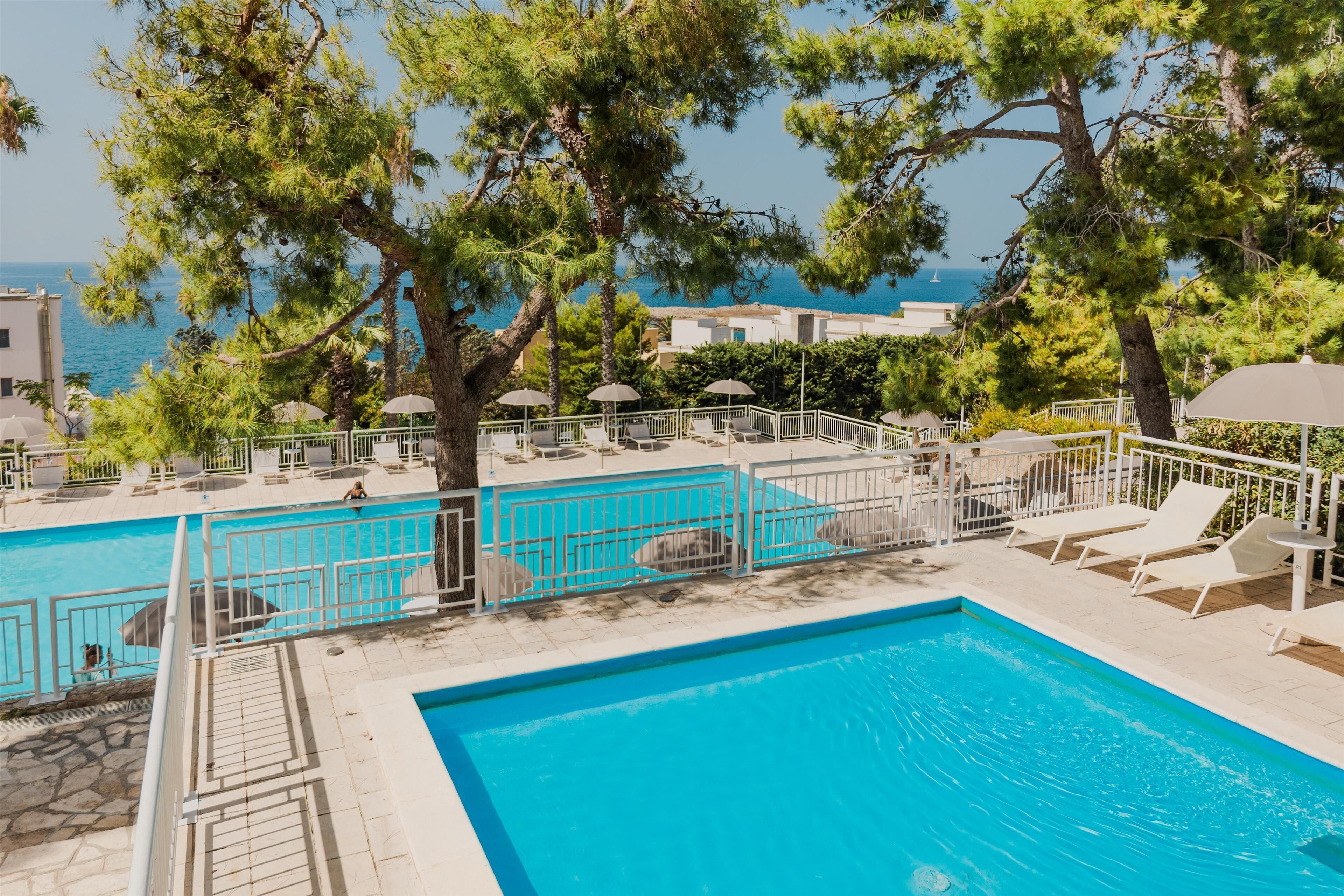 Un espace piscine doté de plusieurs chaises longues et de parasols, entouré d’arbres et offrant une vue sur une étendue d’eau.