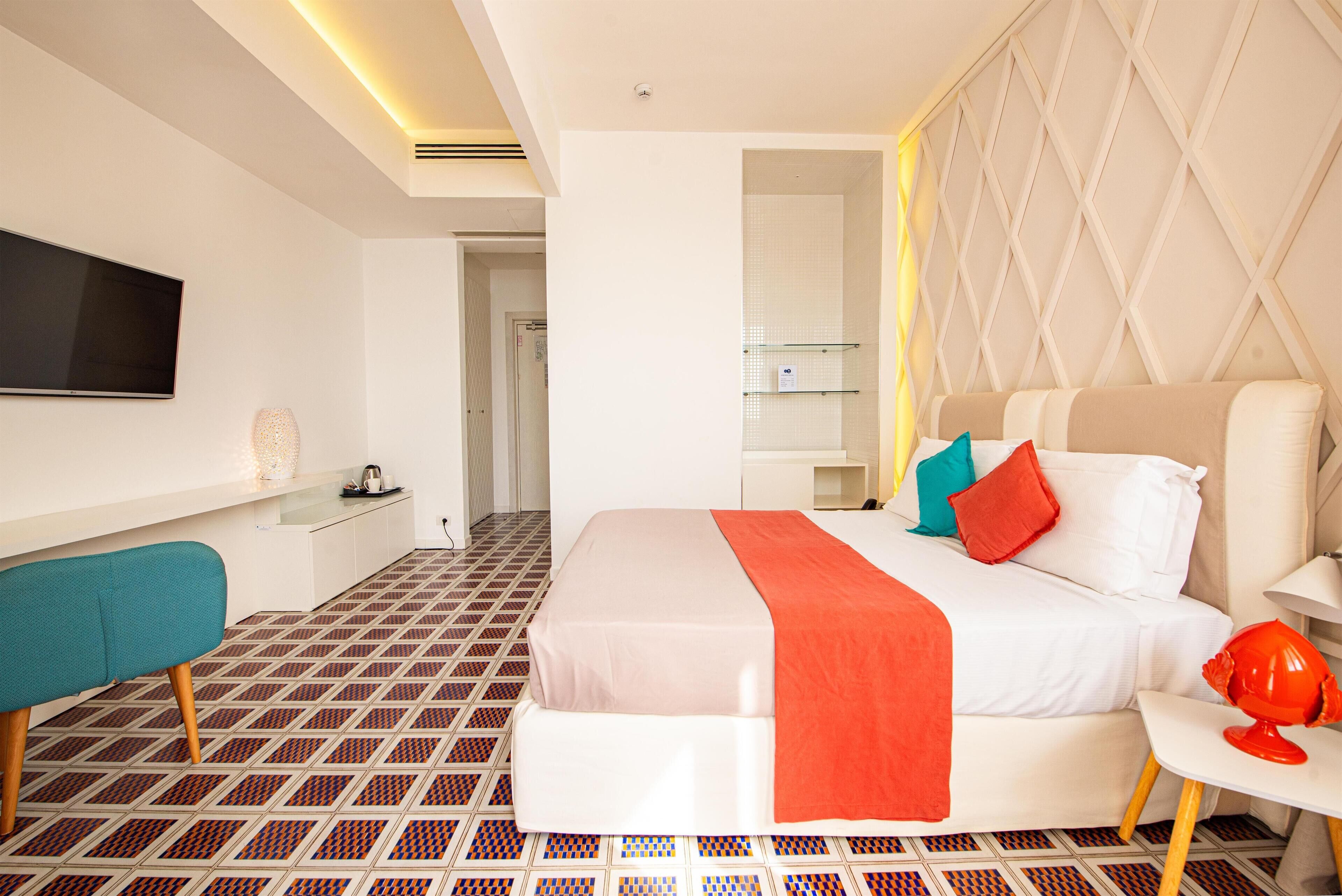 A hotel room with a bed, a TV, a desk, and a patterned floor.