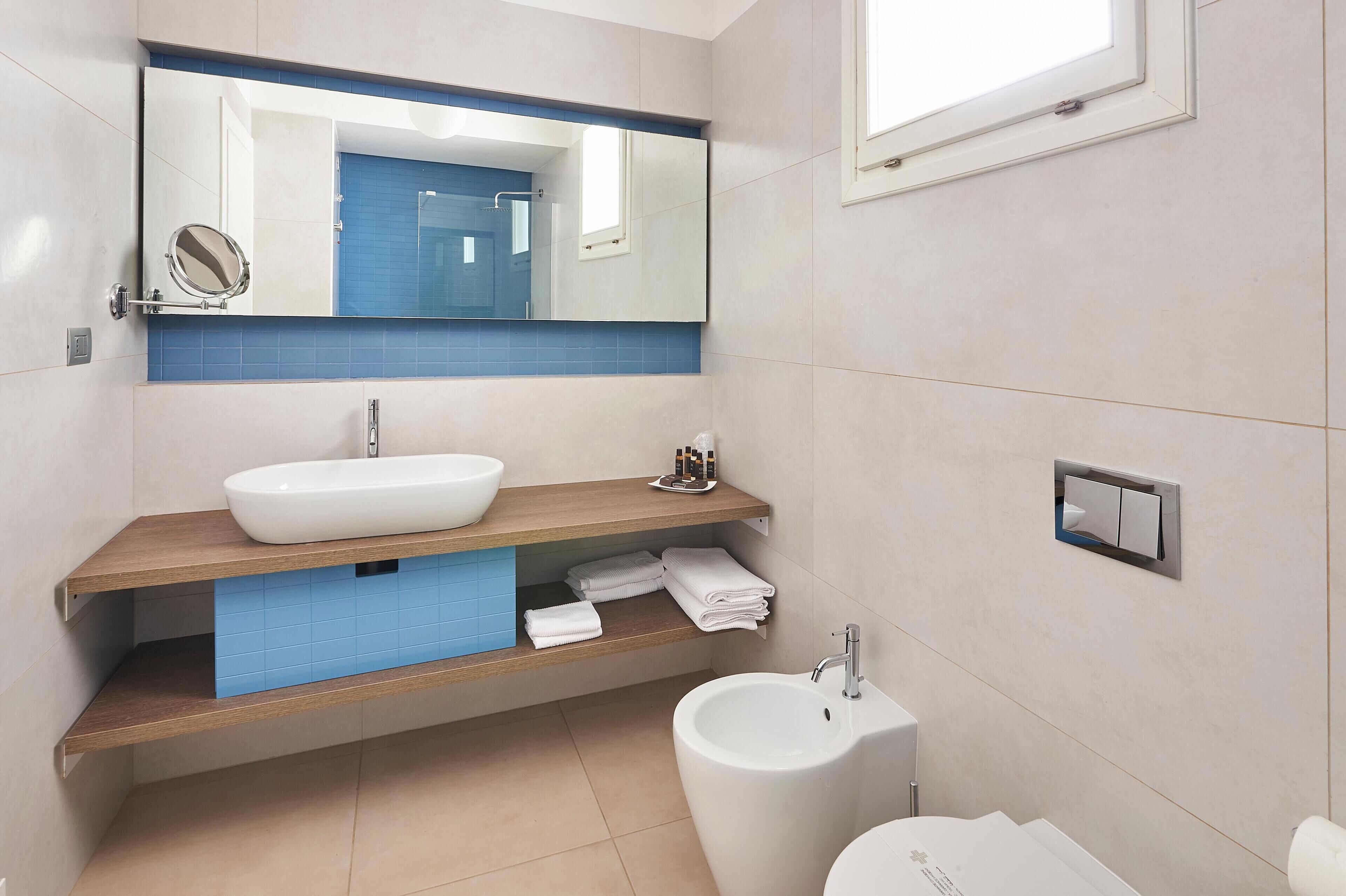 Un bany modern amb un mirall gran, un lavabo blanc, un vàter i un portaToletes.
