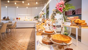 Een buffet met diverse desserts en gebak, een zithoek met stoelen, en een decoratieve bloemstuk.