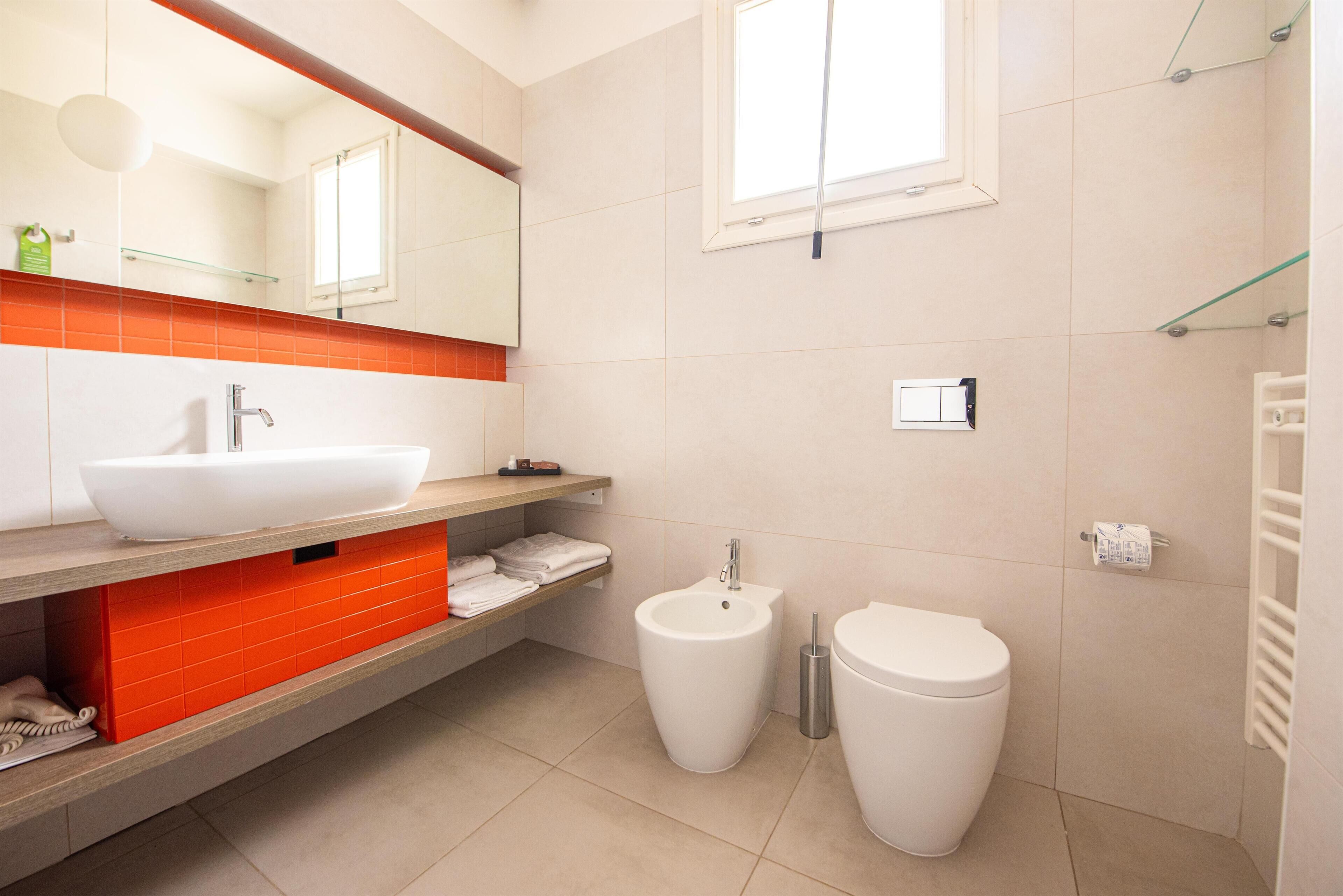Een moderne badkamer met een grote witte wastafel, een hygiëneslot en een toilet.