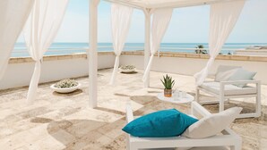 Een terras aan het strand met witte meubels, een kleine tafel en een potplant.