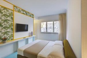 Un dormitorio con cama, televisor montado en la pared, ventana con cortinas y un panel decorativo.