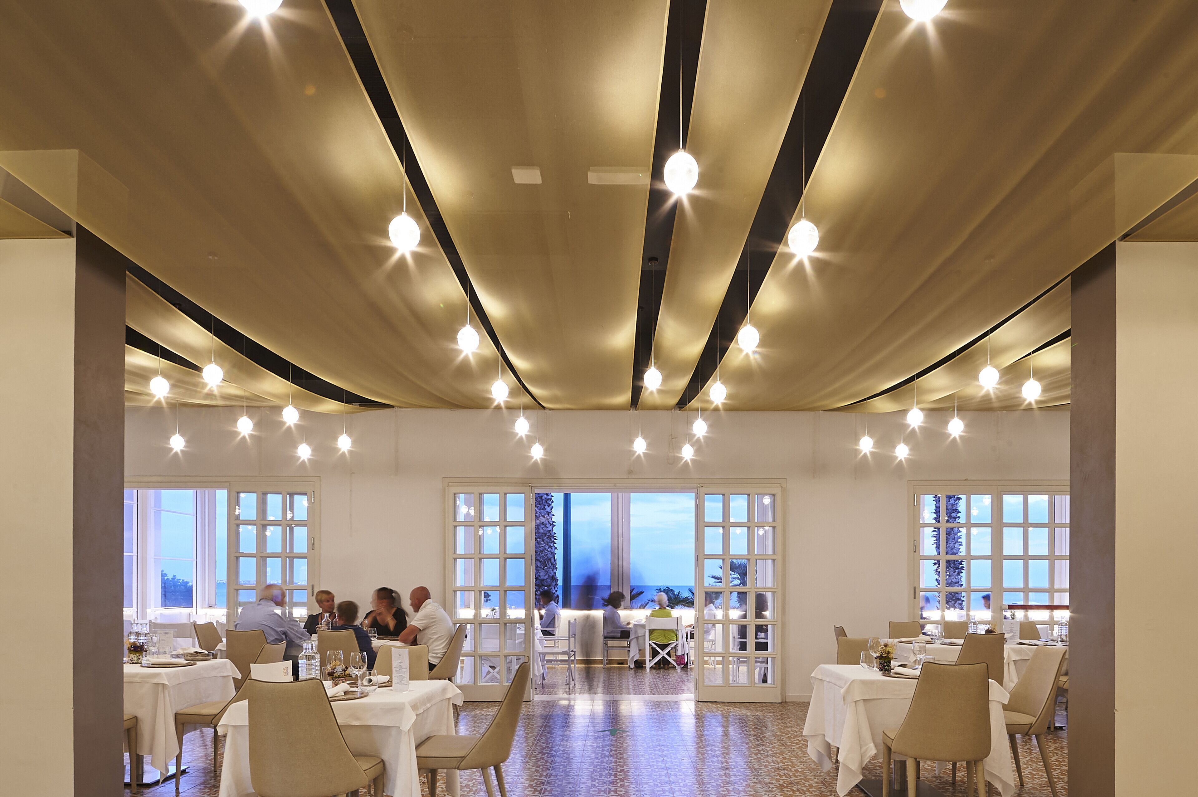 Un comedor amplio con varias mesas y sillas, ventanas grandes con vistas, y un diseño moderno de techo.