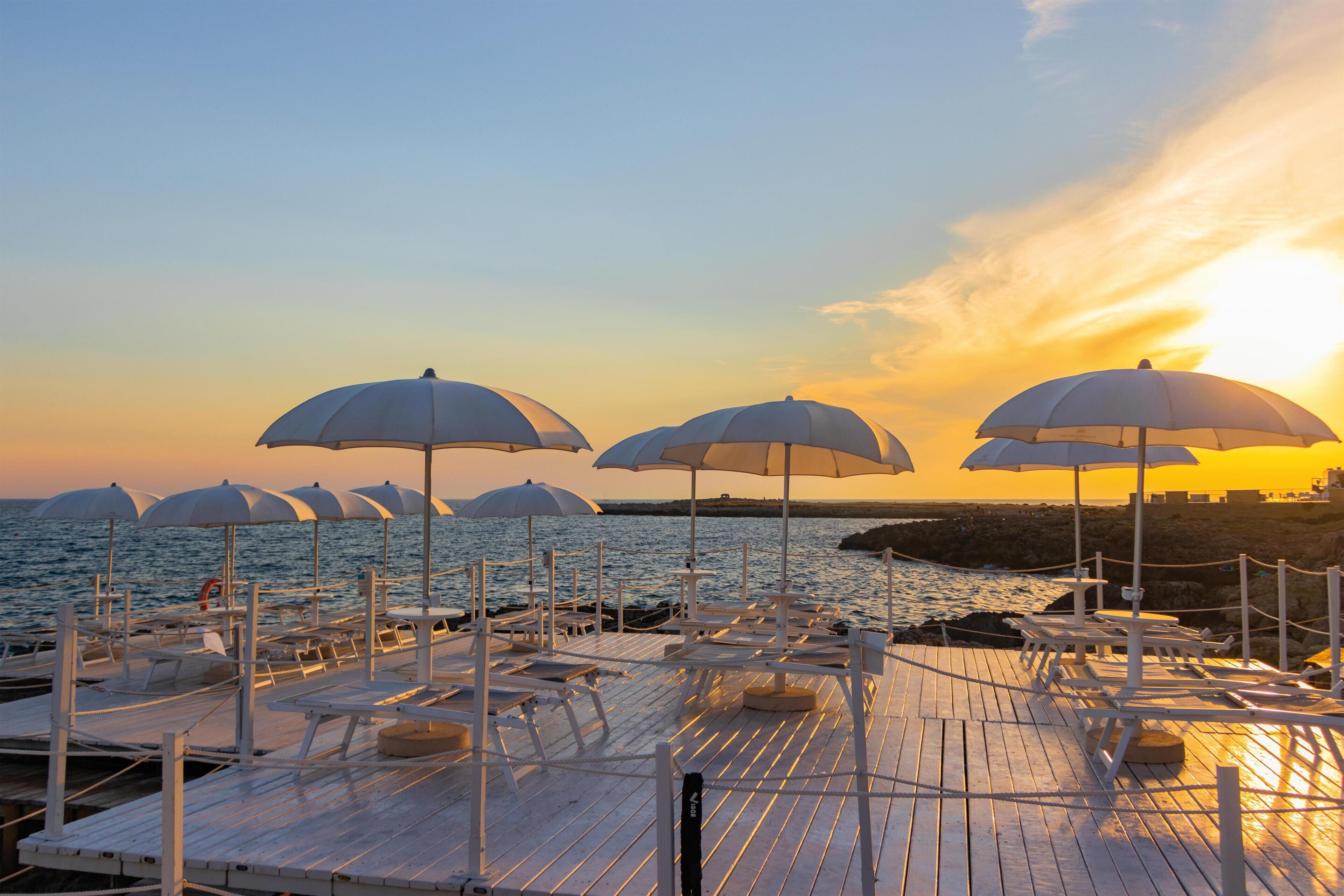 A beachside deck with multiple sun umbrellas and lounge chairs, overlooking the sea.