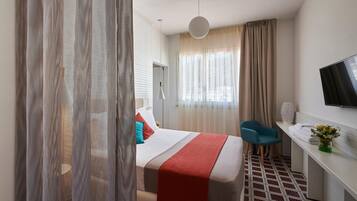 Een hotelkamer met een bed, bureau, stoel, televisie en een raam met gordijnen.