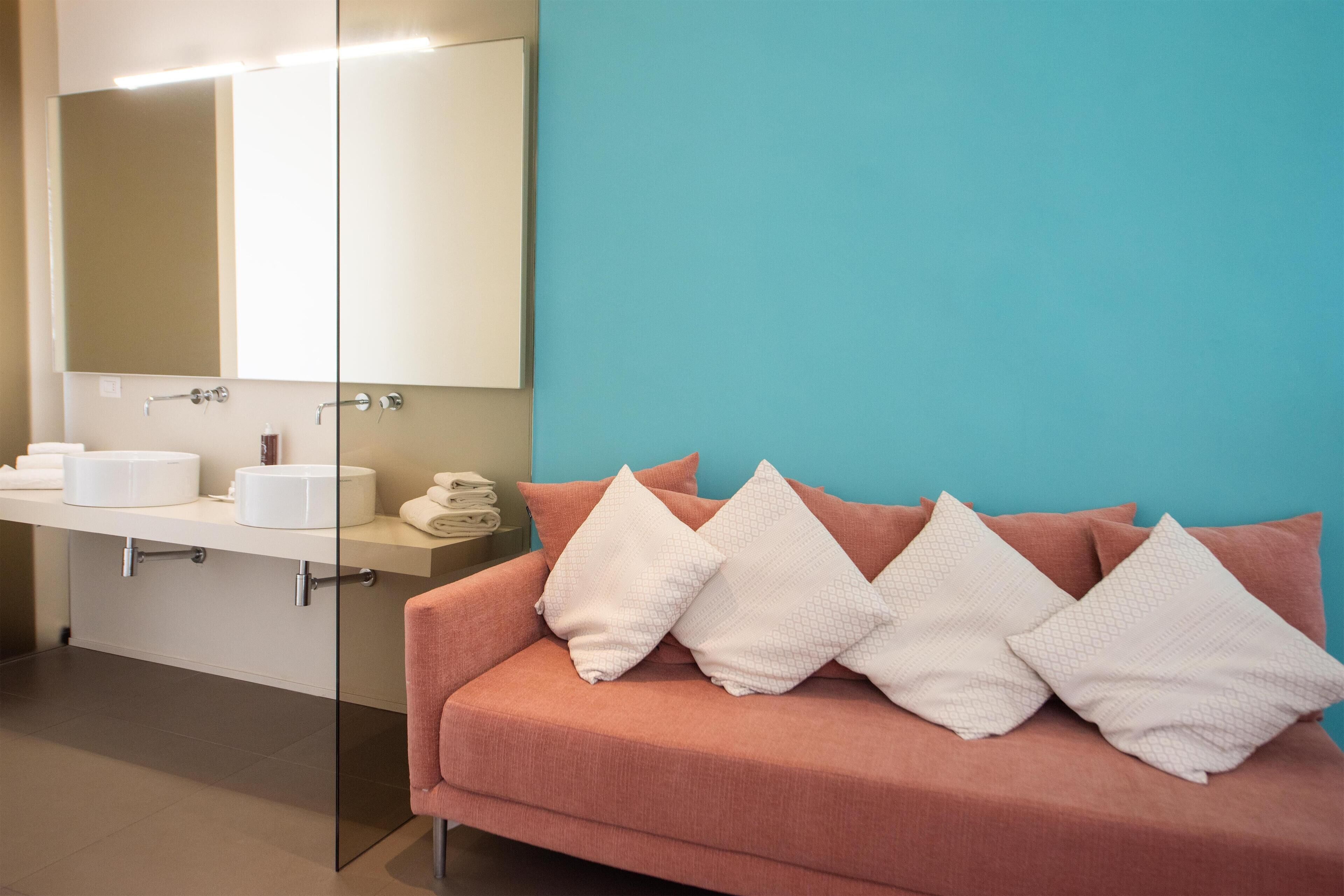 A modern bathroom with a large mirror, a sink, and a pink sofa with white pillows.