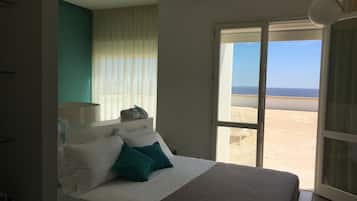 A bedroom with a bed, a window with a view of the beach, and a curtain.