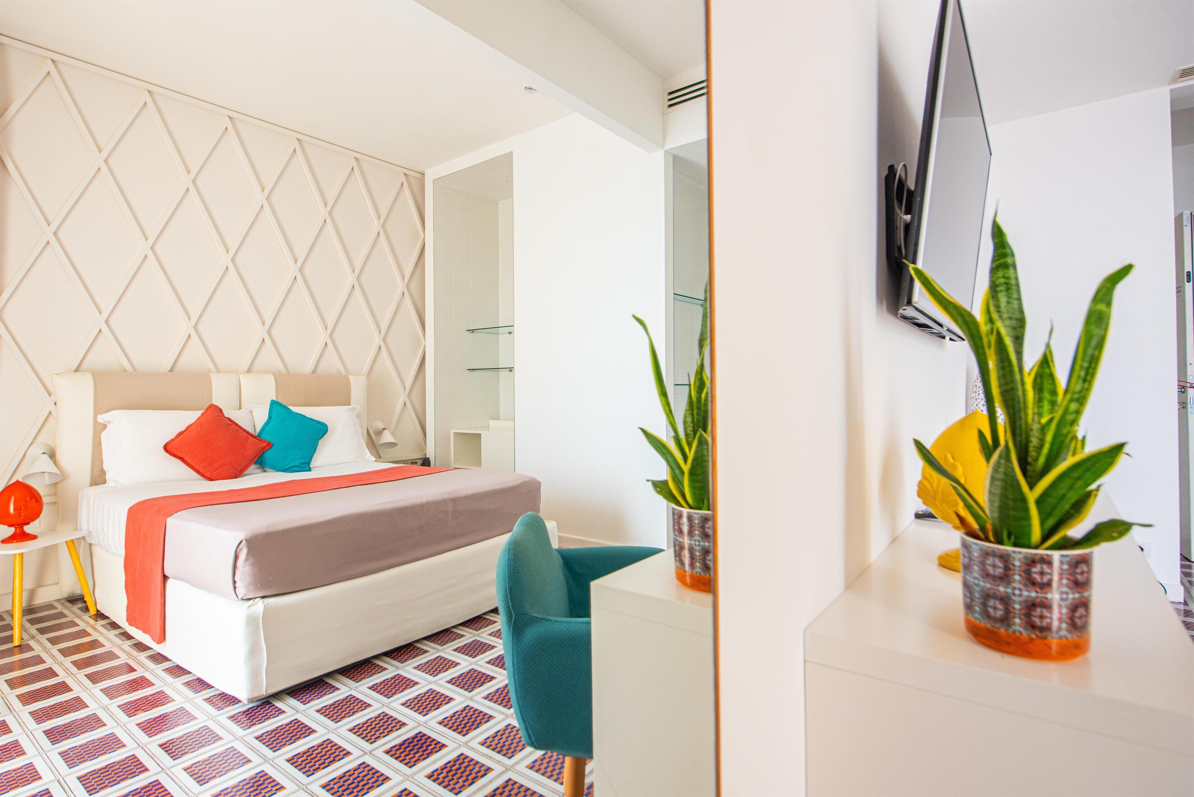 A modern hotel room with a bed, a desk, and two potted plants.