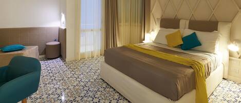 Habitación de hotel con cama, una silla, mesita de noche y ventana con cortinas.