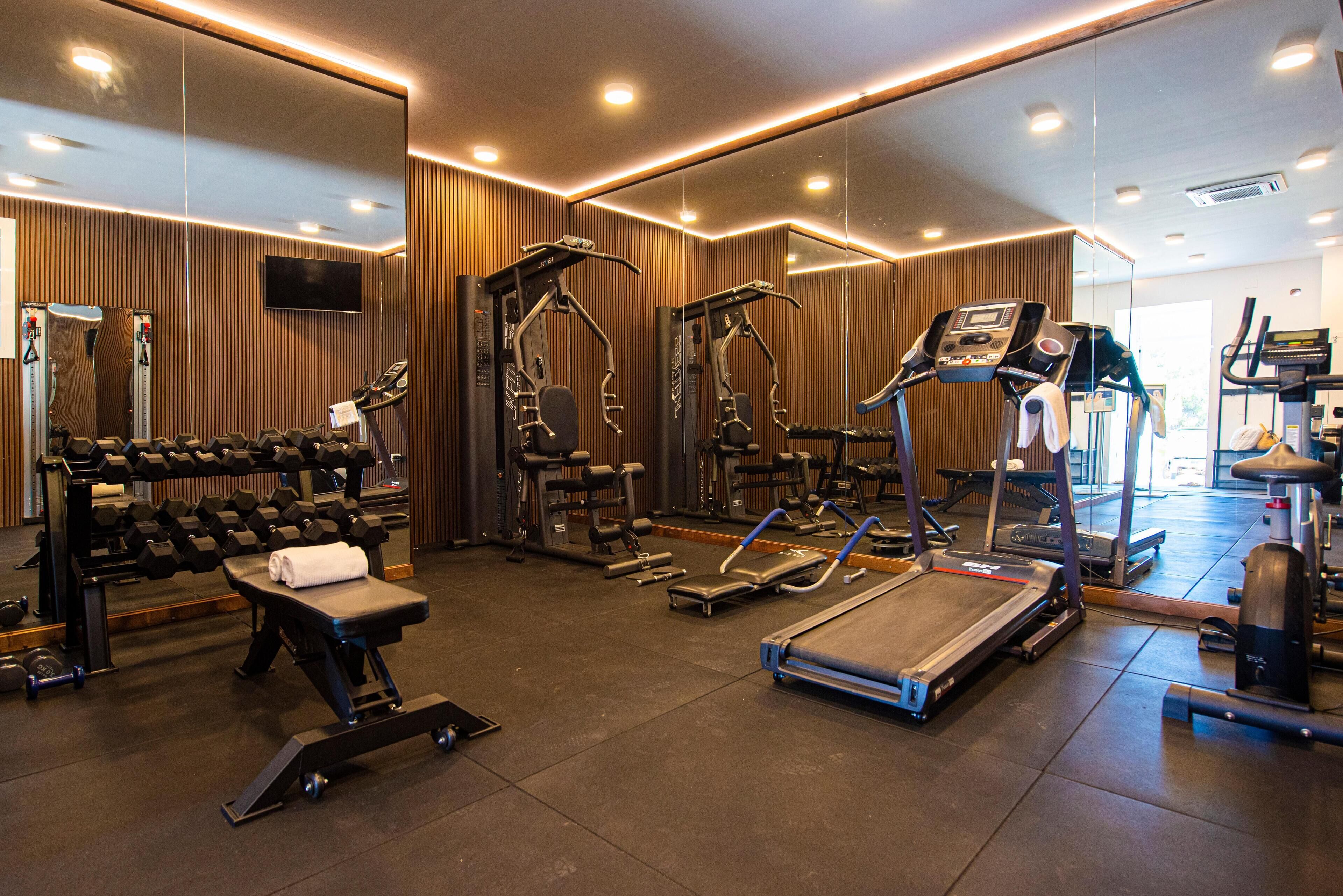 Un gimnasio con diversos equipos de ejercicio, incluyendo cintas de correr, máquinas de pesas y mancuernas.