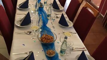 Una larga mesa de comedor dispuesta con servilletas azules, platos y vasos, bordeada por sillas rojas.