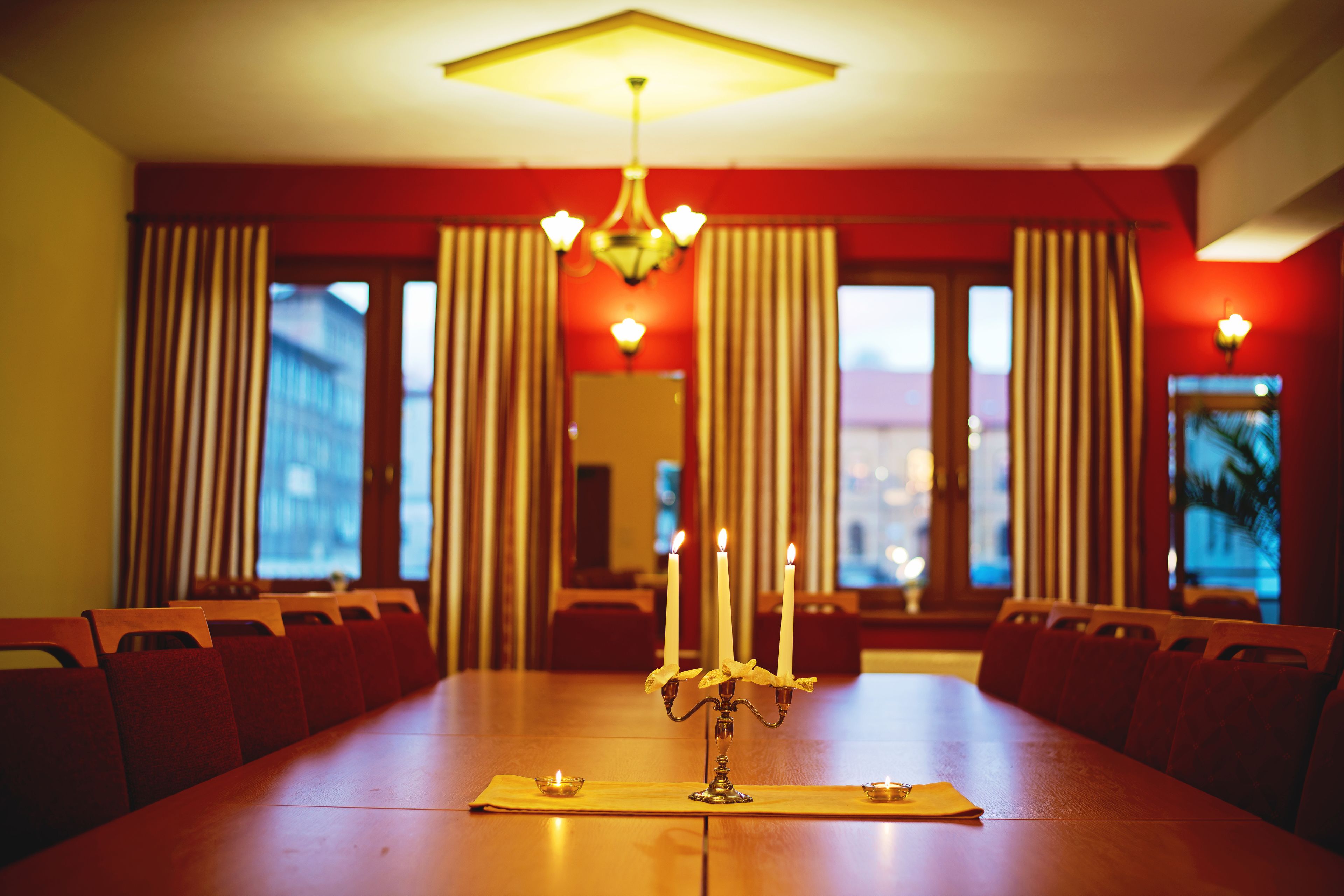 Ein Esszimmer mit einem langen Holztisch, roten Vorhängen und einer Chandelier.