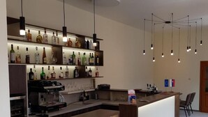 A modern bar area with a long counter, shelves with bottles, and hanging pendant lights. - Tavel Boutique Hotel (Prešov)