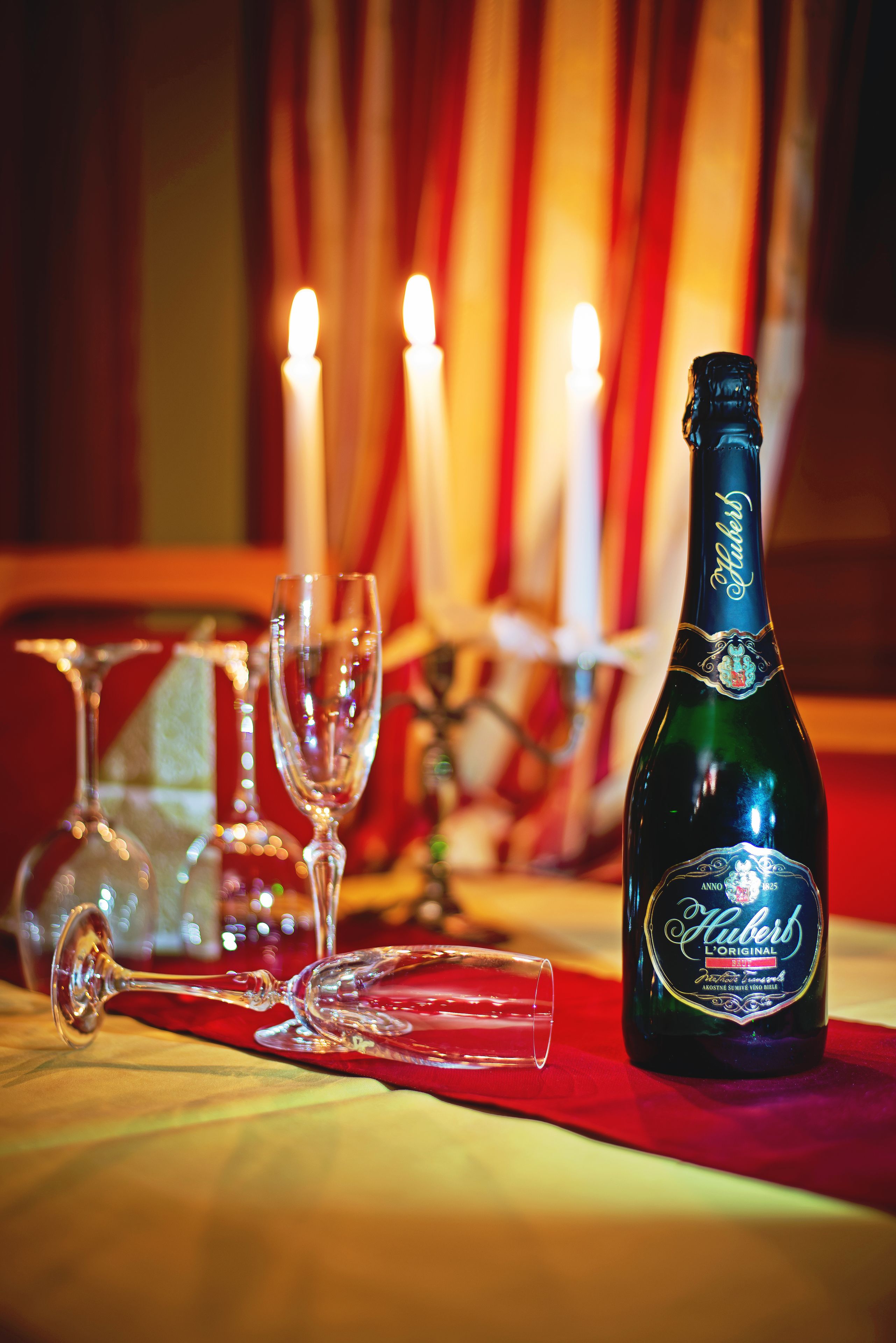 A bottle of champagne, two glasses, and a candle on a table with a red tablecloth.