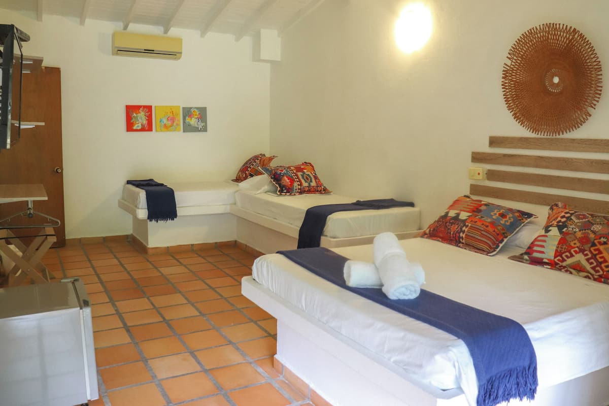 A bedroom with two beds, a wooden headboard, a wall-mounted air conditioner, and three colorful paintings.