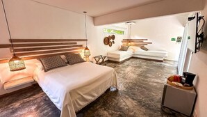 A modern bedroom with a large bed, bedside lamps, a small seating area, and a kitchenette. - Los Colores Ecoparque (Puerto Triunfo)
