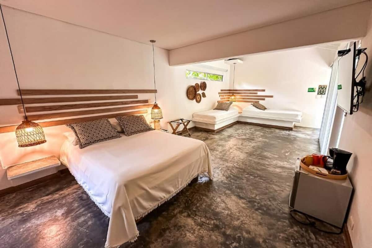 A modern bedroom with a large bed, bedside lamps, a small seating area, and a kitchenette.