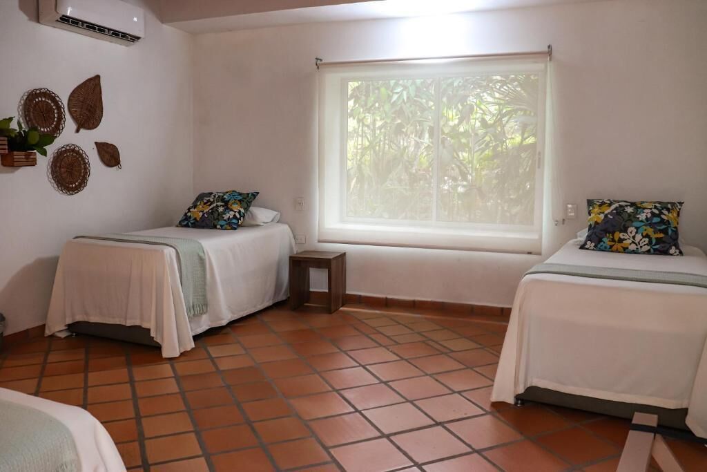 Una habitación con dos camas, una ventana que da a zonas verdes y una mesita.