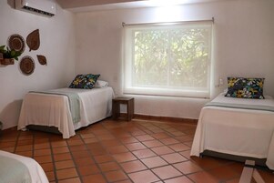 Una habitación con dos camas, una ventana que da a zonas verdes y una mesita.