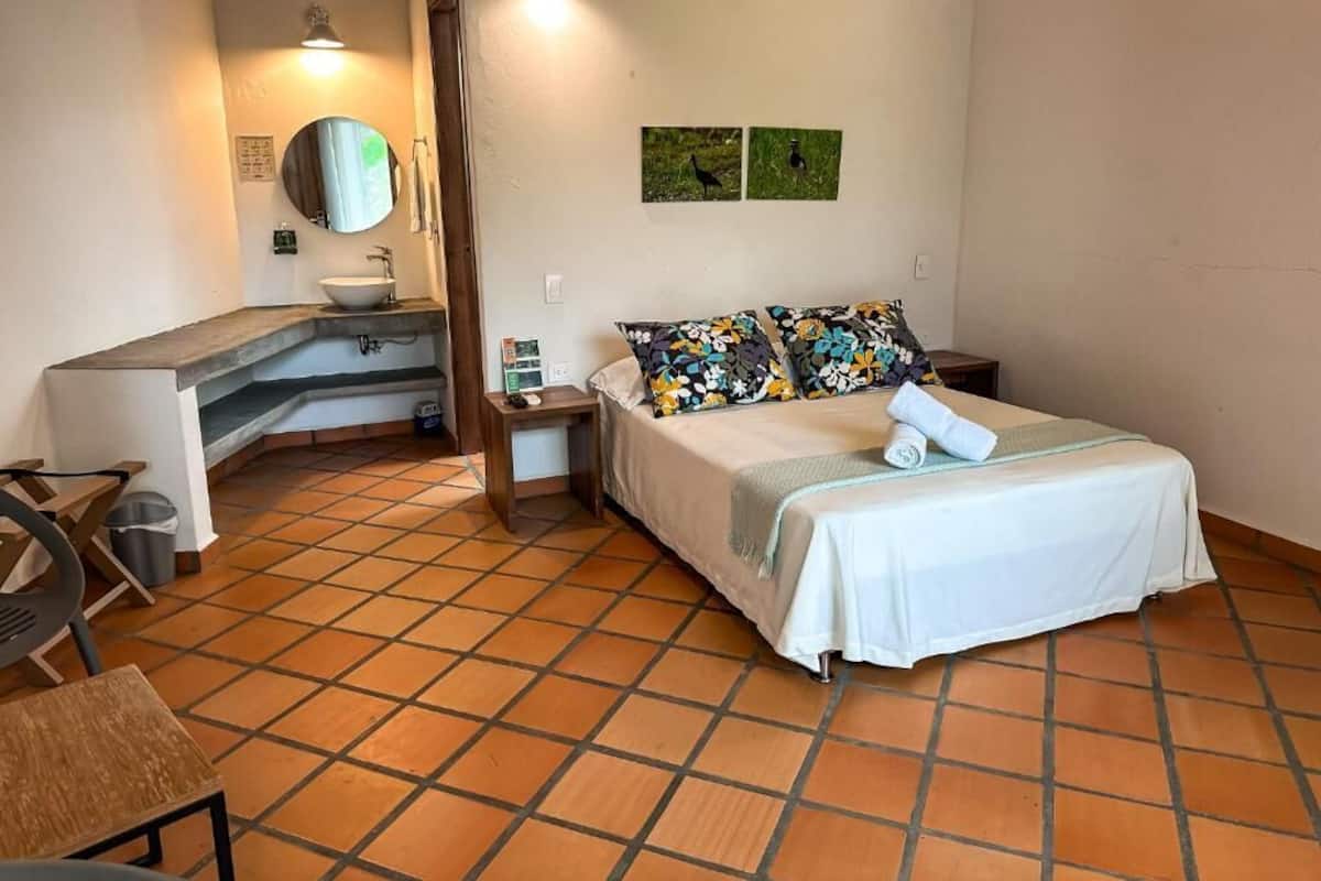A bedroom with a bed, a desk with a sink, a chair, and a mirror.